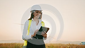 Beautiful caucasian woman in white helmet working with digital tablet at renewable energy farm. Female inspector