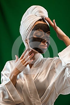 Beautiful caucasian woman in white towel applying black clay mask on her face  on green