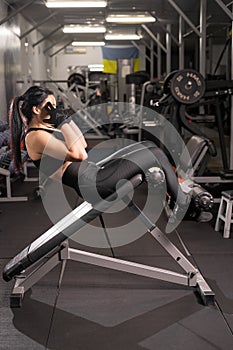 Beautiful caucasian young athletic woman is exercising by doing exercises on the bench in the fitness room. Muscular