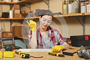 Beautiful caucasian young brown-hair woman working in carpentry workshop at table place.