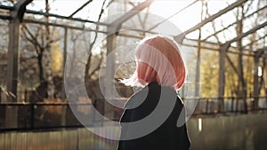 Beautiful caucasian young girl with pink hair and black coat standing at the train station. Attractive woman standing