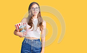 Beautiful caucasian young woman holding popcorn thinking attitude and sober expression looking self confident