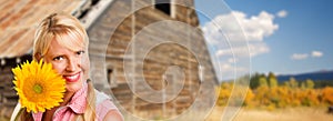 Beautiful Caucasian Young Woman Holding Sunflower In Front of Rustic Barn In The Country