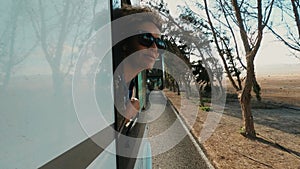 Beautiful caucasian young woman travel outside the car with wind in the curly hair, motion and movement on the road discovering