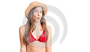 Beautiful caucasian young woman wearing bikini and summer hat scared and amazed with open mouth for surprise, disbelief face