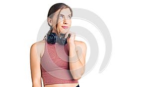 Beautiful caucasian young woman wearing gym clothes and using headphones with hand on chin thinking about question, pensive