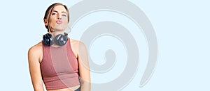 Beautiful caucasian young woman wearing gym clothes and using headphones looking at the camera blowing a kiss on air being lovely