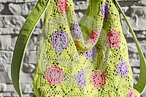 Beautiful ccolorful crocheted handbag with green handle behind the gray stone wall in the garden in summer