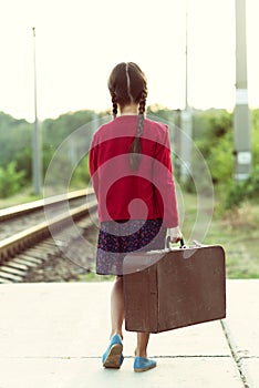 Beautiful charming little girl with pigtails waiting for train at station dressed dark blue dress with flowers and red blouse