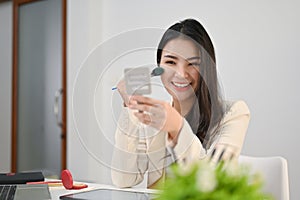 Beautiful Asian businesswoman looking at the mirror and applying makeup on her face