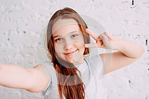 Beautiful charming redhead smiling teenager girl taking selfie on frontal camera isolated on white brick wall