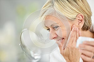 Beautiful charming senior woman putting cream on her face