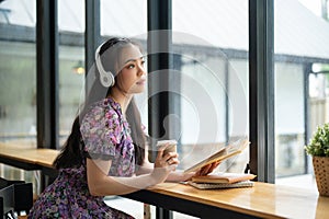 A beautiful Asian woman daydreams while listening to music in a coffee shop photo