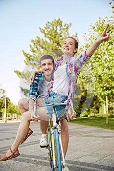 Beautiful cheerful active young couple with bicycle in public park together having fun. Man catches up with girlfriend
