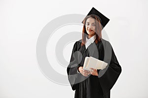 Beautiful cheerful african female graduate smiling holding books looking at camera. Copy space.