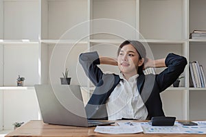 Beautiful and cheerful asian young businesswoman relaxing and stretching her arms and neck after work at her office desk