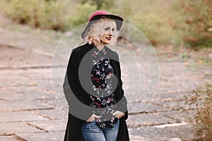 Beautiful cheerful blonde girl with short curly hair in coat and hat walking outdoors on stairs