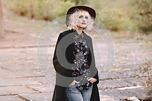 Beautiful cheerful blonde girl with short curly hair in coat and hat walking outdoors on stairs