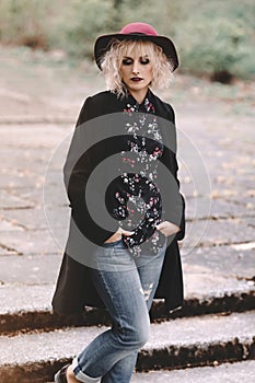 Beautiful cheerful blonde girl with short curly hair in coat and hat walking outdoors on stairs