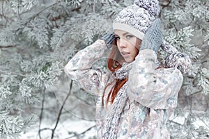 Beautiful cheerful cute red-haired girl in a cap and scarf plays with snow in the beautiful forest fairy