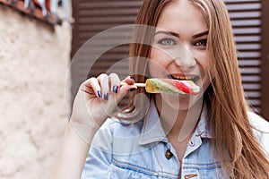 Beautiful cheerful cute red-haired girl eating colored ice cream on city streets