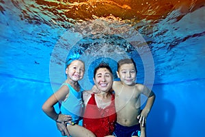 A beautiful, cheerful family: a mother, a young son and daughter, swimming and posing underwater in the pool. They look