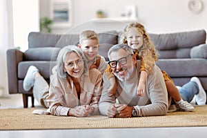 Beautiful cheerful family two cute little kids hugging with positive senior grandparents on floor