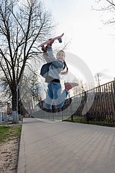 Beautiful cheerful girl in denim and pink sneakers jumps up and holds penny board,  longboard above her head.