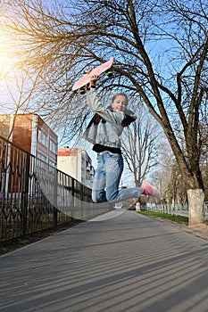 Beautiful cheerful girl in denim and pink sneakers jumps up and holds penny board,  longboard above her head.