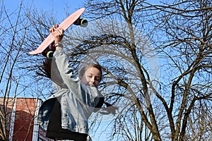 beautiful cheerful girl in denim and pink sneakers jumps up and holds penny board, longboard above her head. International