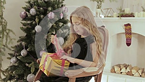 Beautiful, cheerful girl opens her gift on the background of the Christmas tree