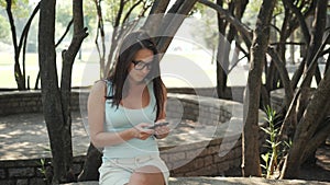 Beautiful Cheerful Girl With a Smartphone Sitting In a Park on a Bench on a Sunny Day, On-line Shopping Concept