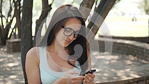 Beautiful Cheerful Girl With a Smartphone Sitting In a Park on a Bench on a Sunny Day, On-line Shopping Concept