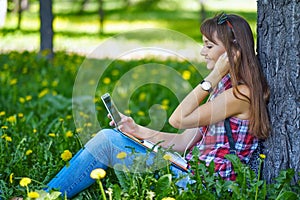 Beautiful cheerful girl with a smartphone sitting in a park on a bench on a sunny dayteenager, on-line shopping concept