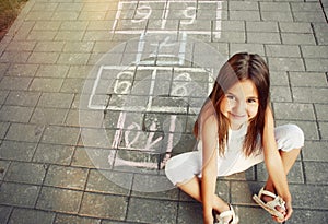 Beautiful cheerful little girl playing hopscotch on playground