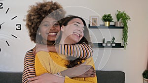 Beautiful and cheerful multiracial lesbian couple hugging at their apartment. Two lovely and happy homosexual women