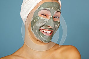 Beautiful cheerful teen girl applying facial clay mask. Beauty treatments,  on blue background