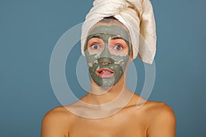 Beautiful cheerful teen girl applying facial clay mask. Beauty treatments,  on blue background