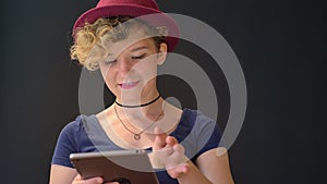 Beautiful cheerful woman with curly blonde hair browsing on tablet and smiling at camera, isolated on black background