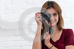 Beautiful cheerful woman holding camera and focusing on you with smile while standing against white background. Portrait of