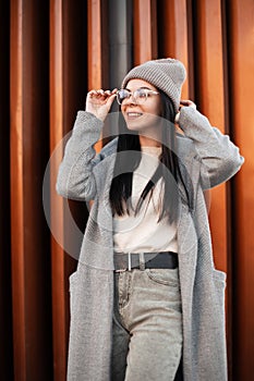 Beautiful cheerful young hipster woman with cute smile in fashionable clothes straightens glasses. Fashion portrait happy girl