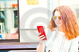 A beautiful cheerful young red-haired woman is having a good time in the Park on a beautiful day, communicating on a mobile device