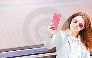 A beautiful cheerful young red-haired woman is having a good time in the Park on a beautiful day, taking selfies