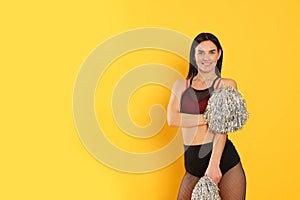 Beautiful cheerleader in costume holding pom poms on yellow background. Space for text