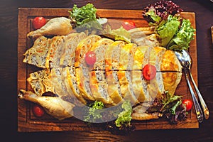 Beautiful chicken and mushroom pie with herbs, tomatoes and chicken legs on a wooden board in a restaurant. Selective focus, close