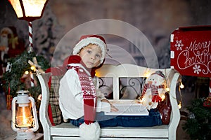 Beautiful child, blond toddler boy, reading a book, sitting on a bench with christmas decoration