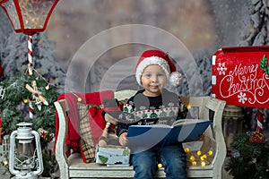 Beautiful child, blond toddler boy, reading a book, sitting on a bench with christmas decoration