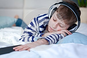 Beautiful child boy lies on the bed and listens to music and enjoys. He closed his eyes from dreams or fell asleep