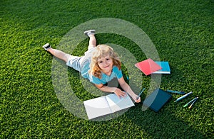 Beautiful child boy writing on notebook on grass background. Kids reading book in park. Concept of kids learning, study