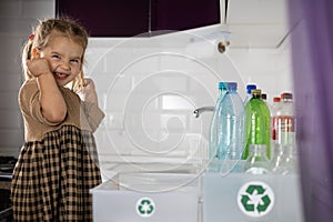 A beautiful child clenches his fists victoriously after sorting plastic for recycling. A little girl is happy to help
